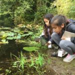 Two School Overnight Program students bend down to explore Mac's Pond.