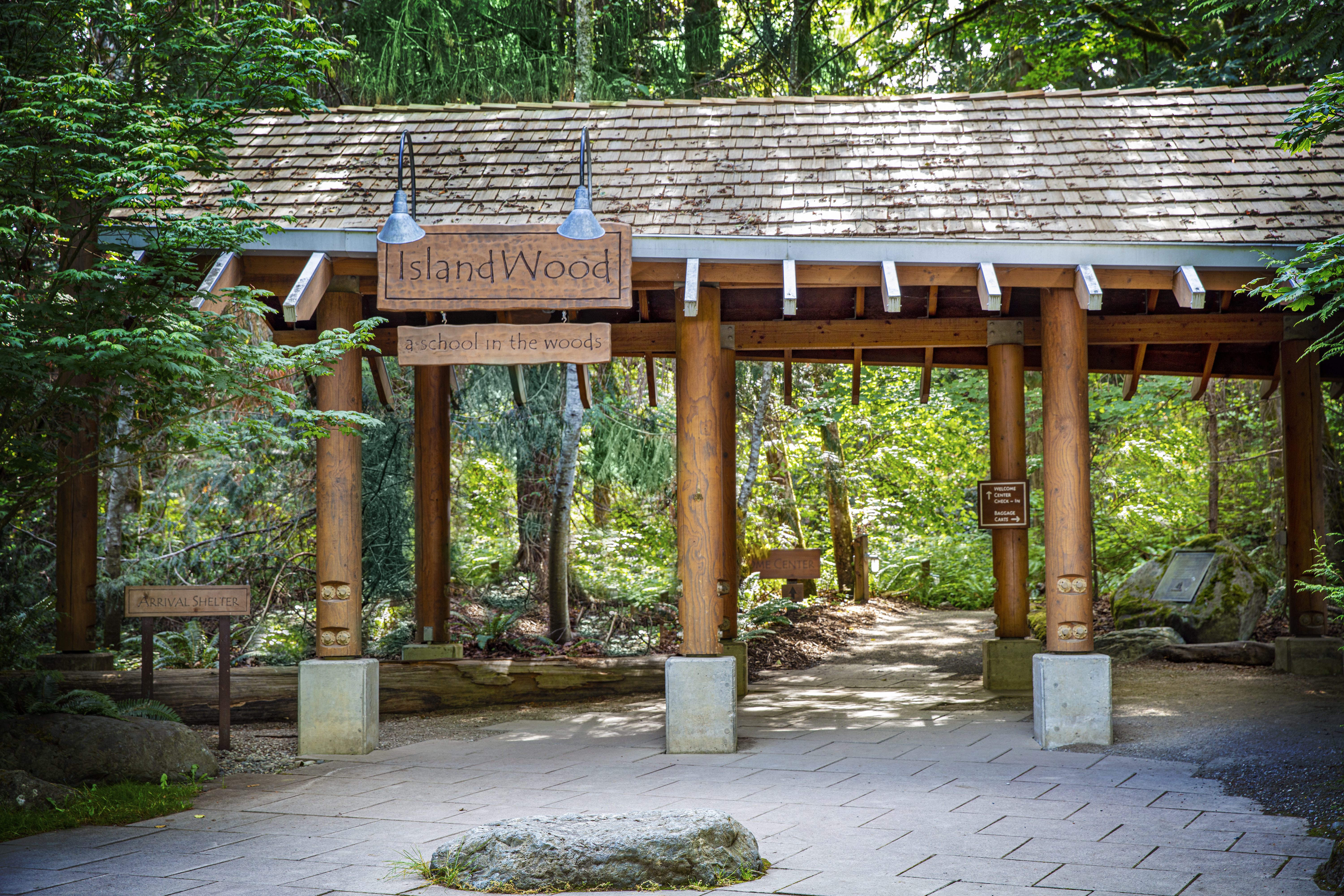 The Arrival Shelter at IslandWood's Bainbridge Island campus. A wood sign says "IslandWood," with a smaller wood sign below it, which says "A school in the woods."