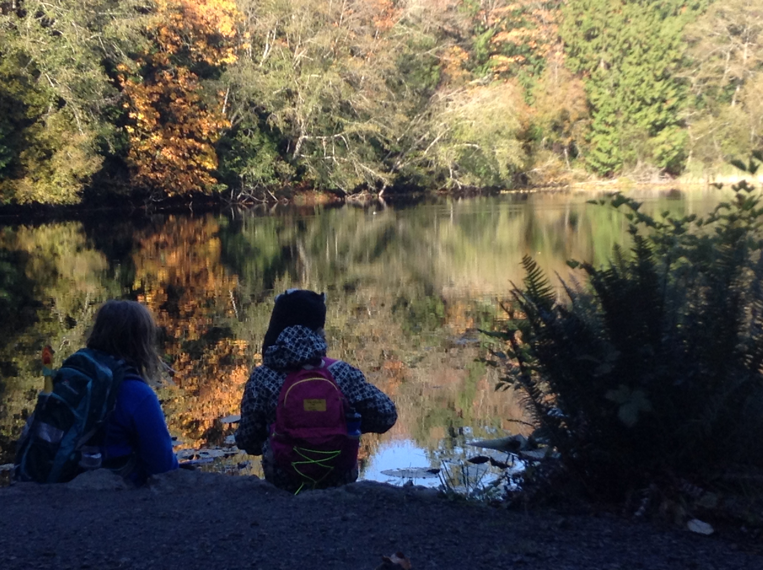 Two students sit on the bank of Mac's Pond.