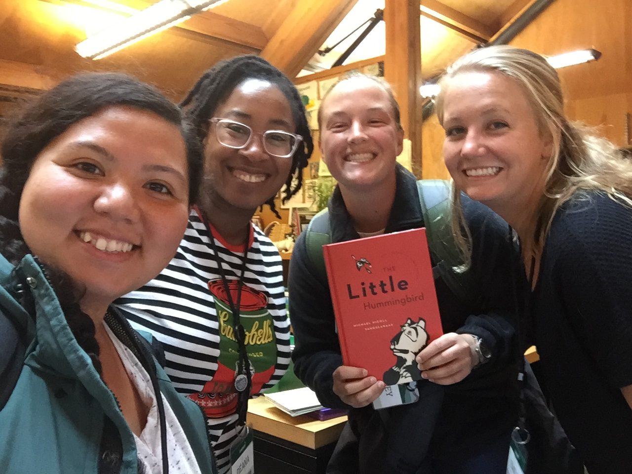 Déana Scipio smiles for the camera with three students from the IslandWood Graduate Program. One of the students holds up a children's book.
