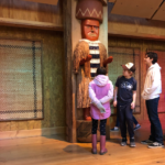 [Image description: three students stand in front of the house post in IslandWood's Great Hall.]