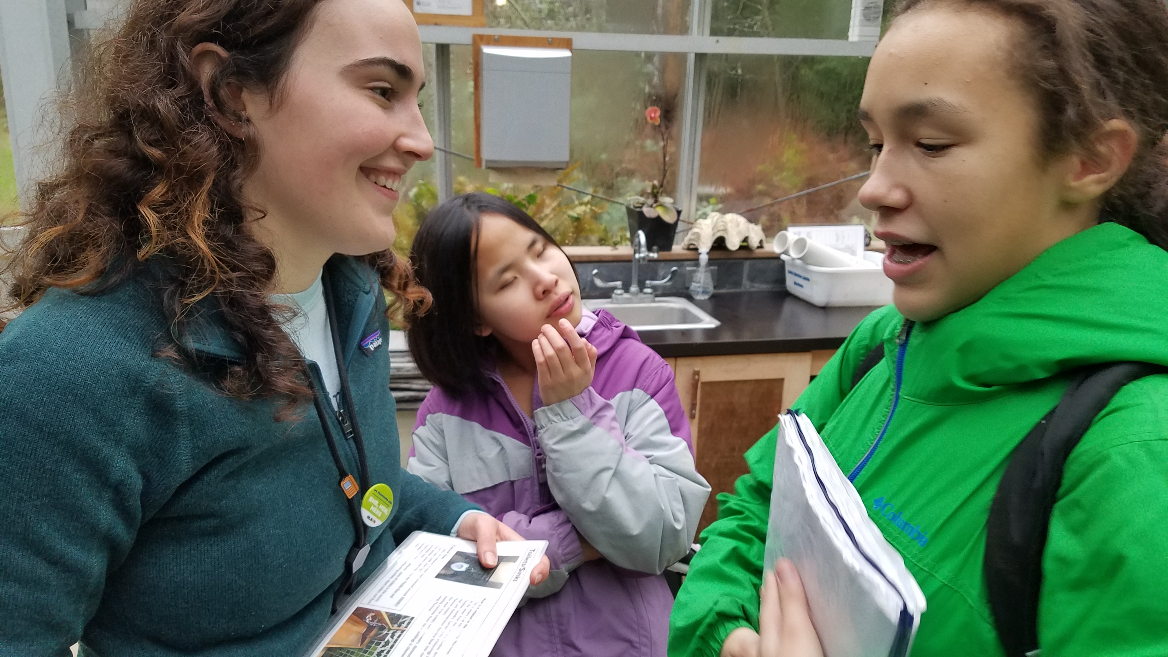 [Image description: IslandWood graduate student and School Overnight Program instructor Taylor O'Connor smiles as she talks to two students from the Washington State School for the Blind.]